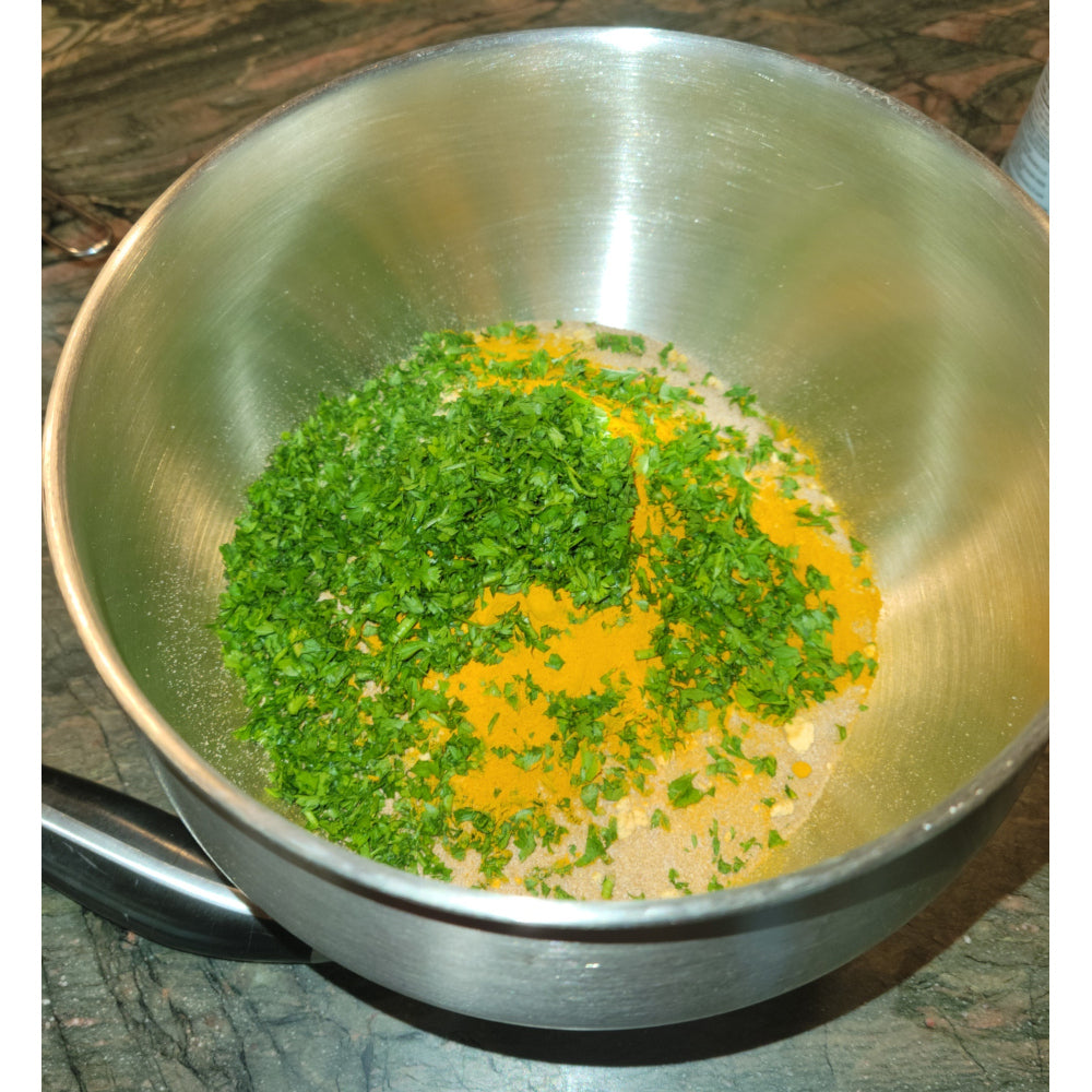 A stainless steel mixing bowl filled with fresh, natural dry ingredients like parsley and turmeric, showcasing the wholesome recipe.