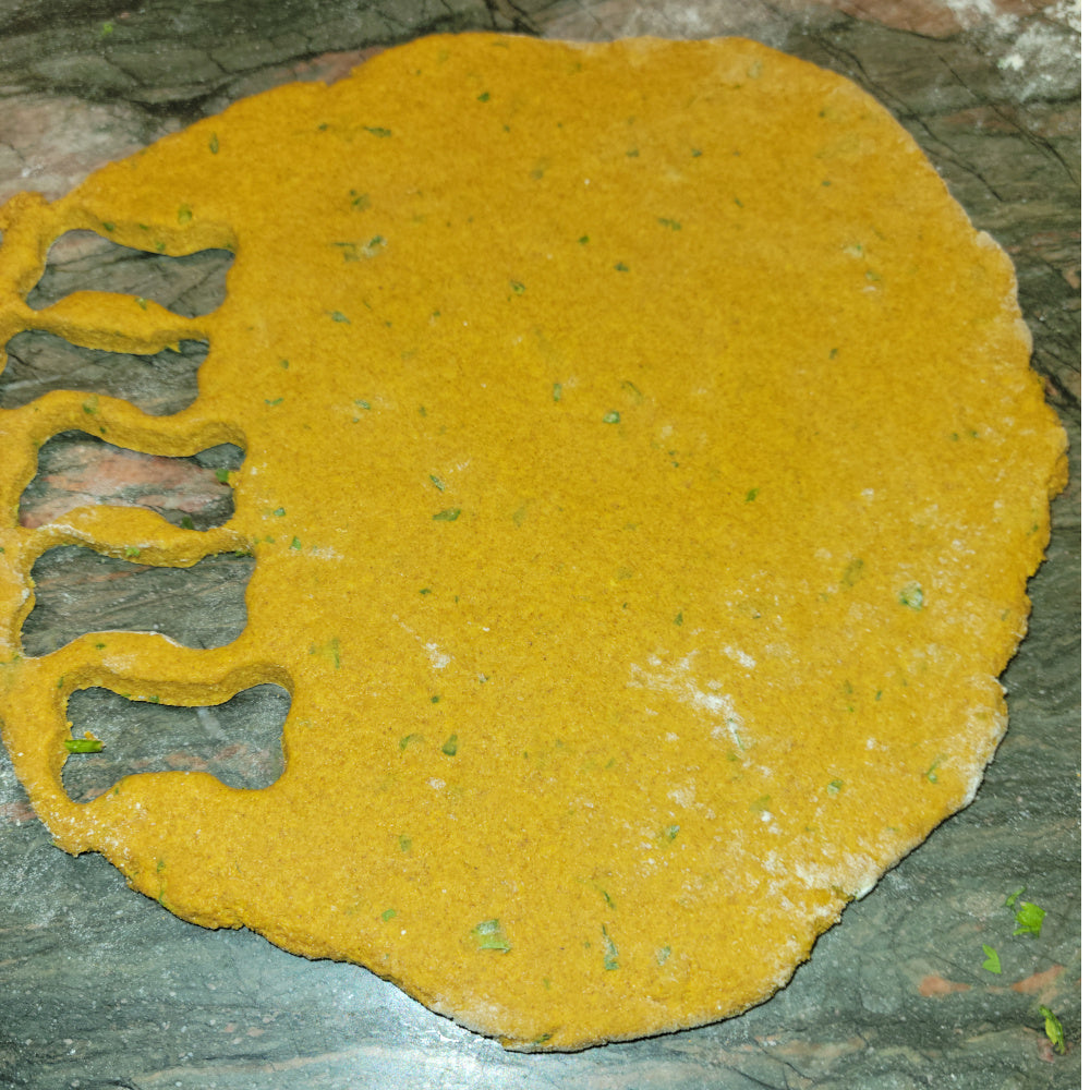 Golden dough rolled flat on a counter with small bone shapes cut out, highlighting the small-batch, handmade quality of the biscuits.