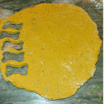 Golden dough rolled flat on a counter with small bone shapes cut out, highlighting the small-batch, handmade quality of the biscuits. Thumbnail