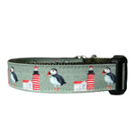 Adjustable nylon webbing dog collar featuring a repeating pattern of puffins and red-and-white striped lighthouses on a sage green background, complete with a black plastic side-release buckle. Thumbnail