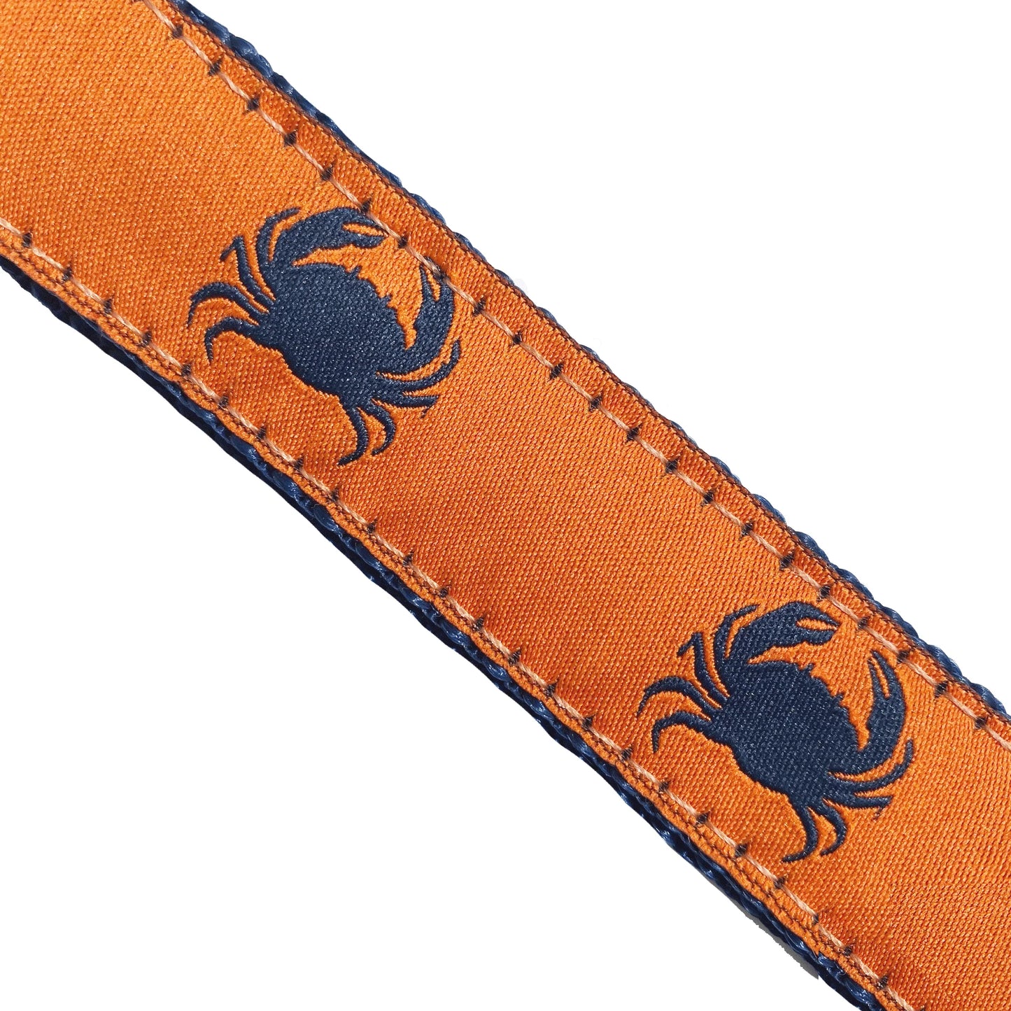 Extreme close-up of the dog collar's fabric, displaying the repeating navy blue crab motif on a bright orange ribbon, highlighting the precise, heavy-duty edge stitching that ensures durability.