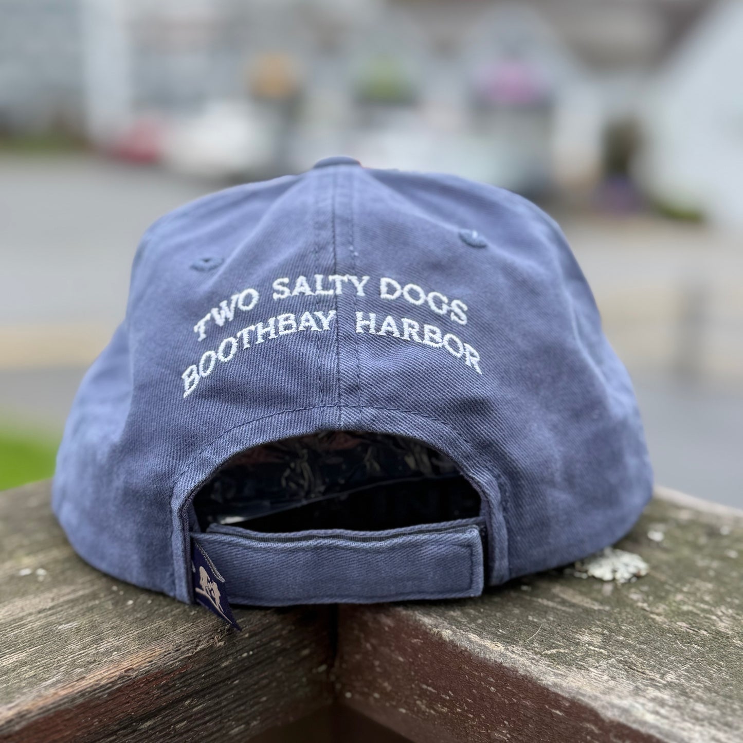 Blue cap with 'Two Salty Dogs Boothbay Harbor' text on a wooden surface