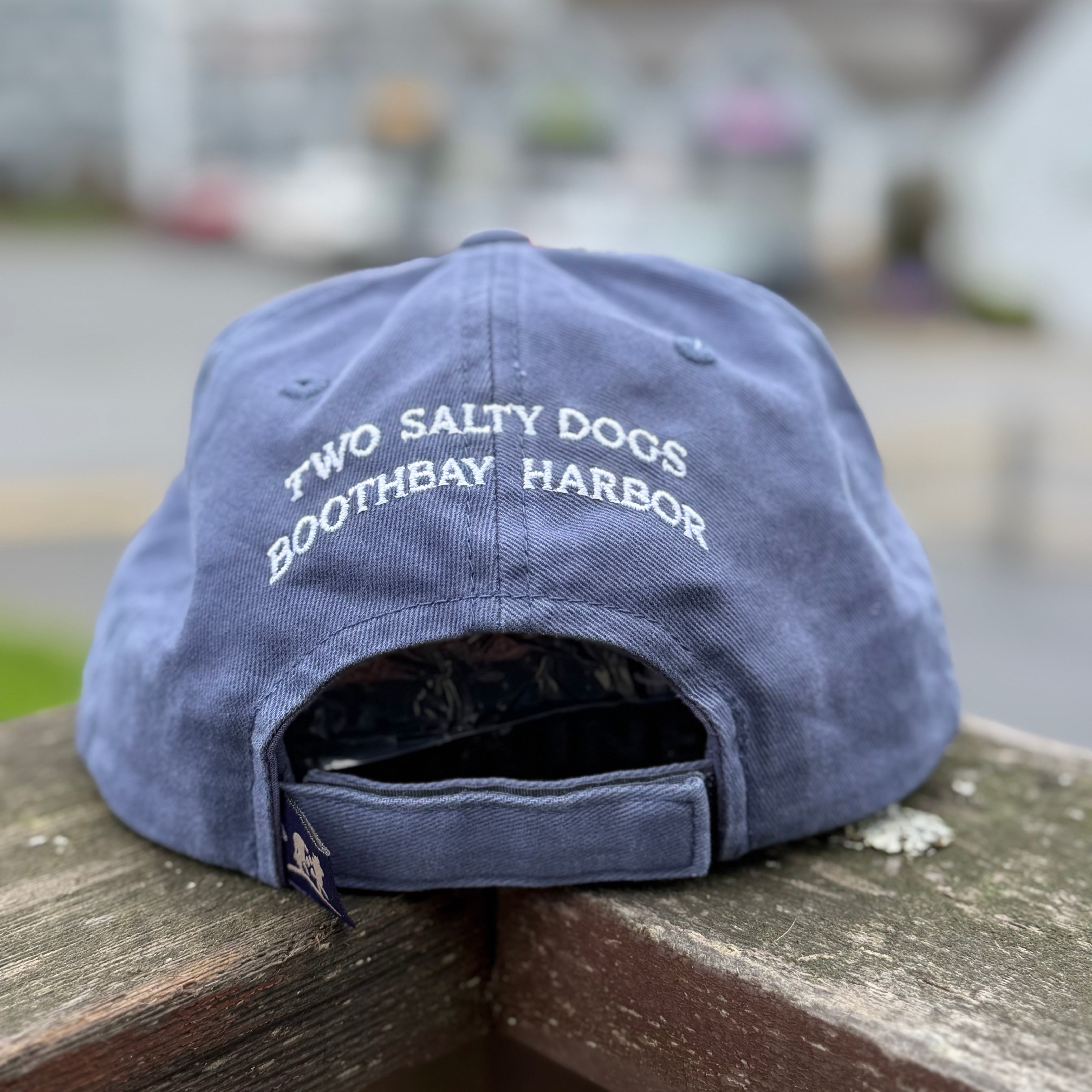 Blue cap with 'Two Salty Dogs Boothbay Harbor' text on a wooden surface