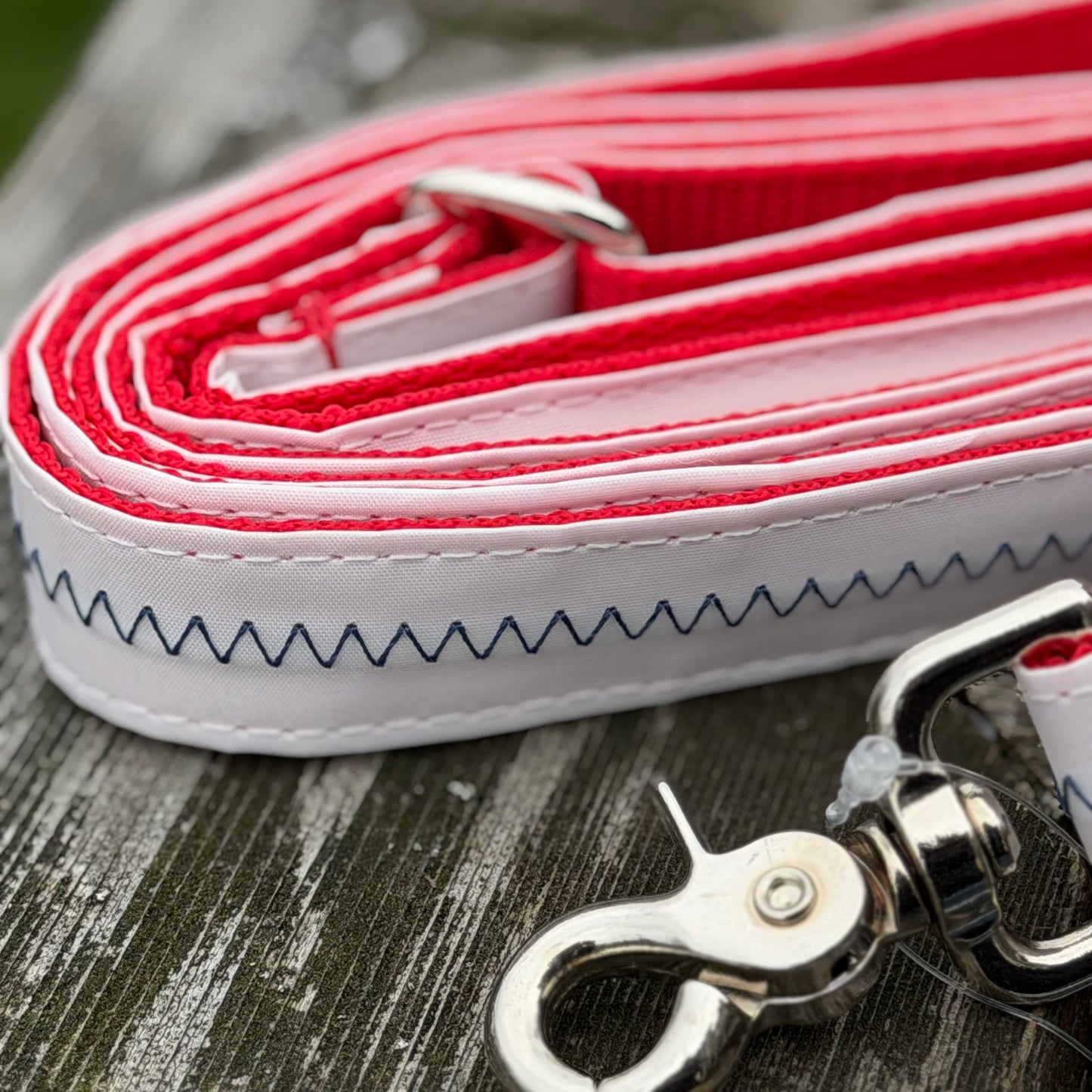 Extreme close-up of a recycled sailcloth dog leash detailing the durable white Dacron material, heavy-duty blue stitching, bright red nylon webbing, and rust-proof snap hook.