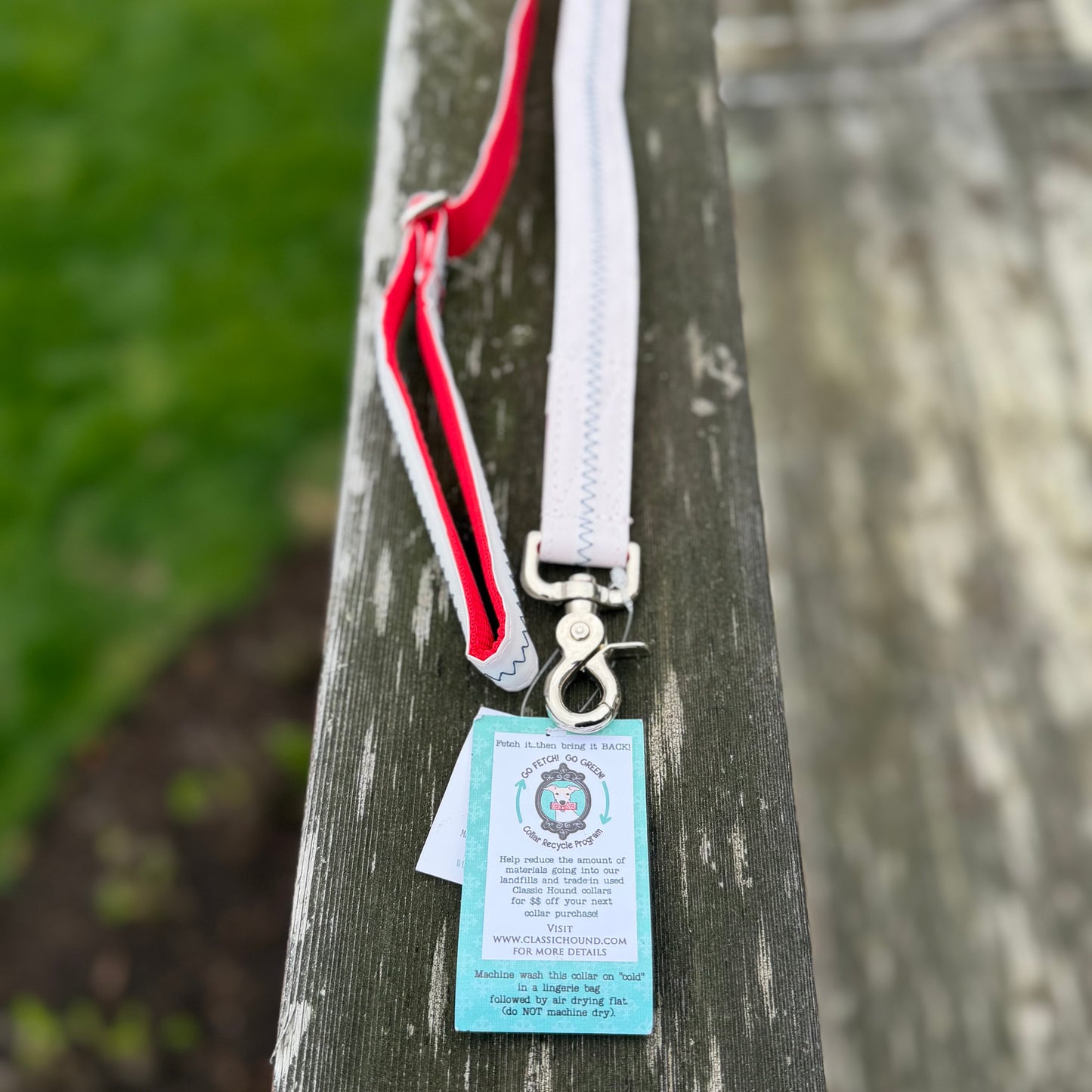 6ft white recycled Maine Dacron sailcloth dog leash hanging outdoors, displaying the adjustable handle, red nylon webbing, and durable metal hardware.
