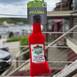 Red plush cat toy resembling a bottle with a label on a metal railing, against an outdoor background. Thumbnail