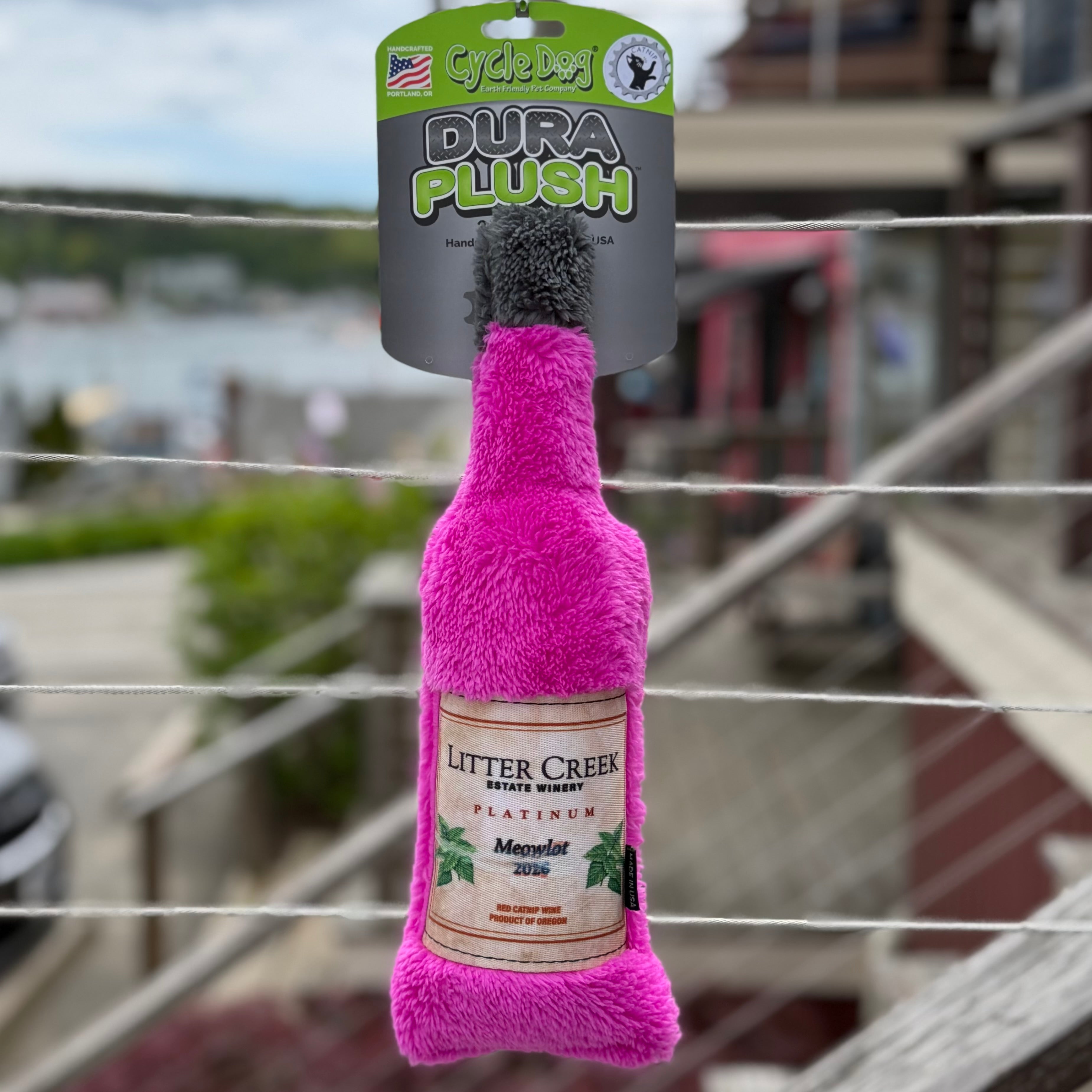 Cycle Dog Dura Plush wine bottle cat toy with "litter creek" text hanging with a blurry background