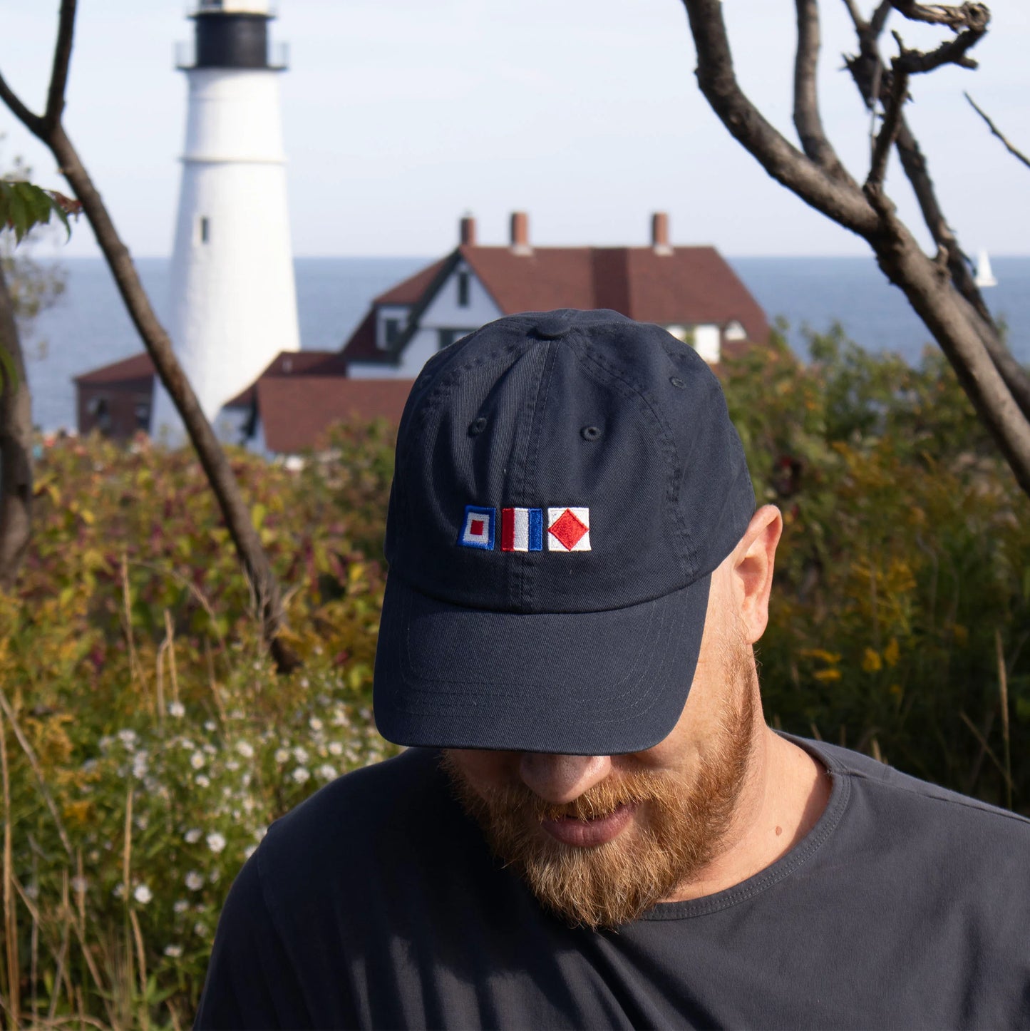Man wearing a washed navy blue baseball cap with nautical flags on the front that spell WTF