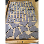 A Parchment-lined baking sheet filled with unbaked treats cut into fun, bite-sized bone and state of Maine shapes. Thumbnail