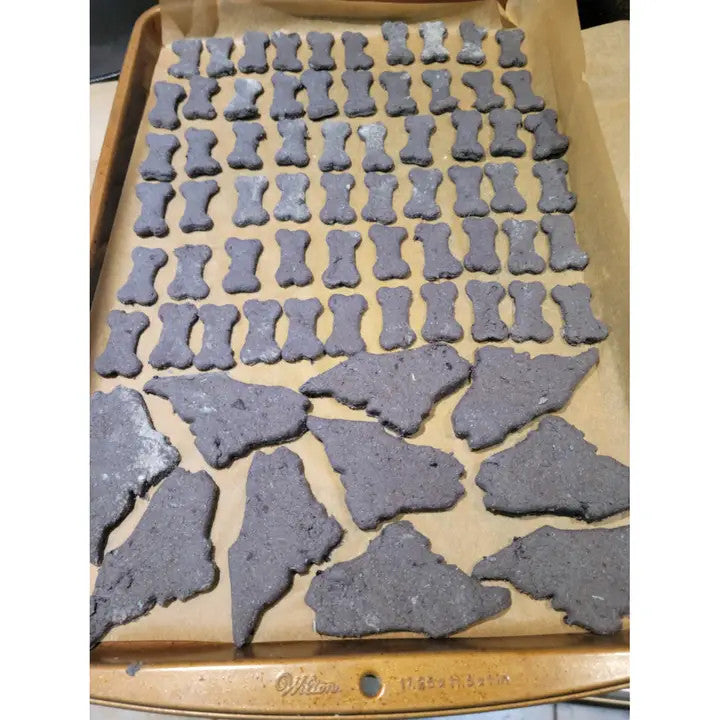 A Parchment-lined baking sheet filled with unbaked treats cut into fun, bite-sized bone and state of Maine shapes.