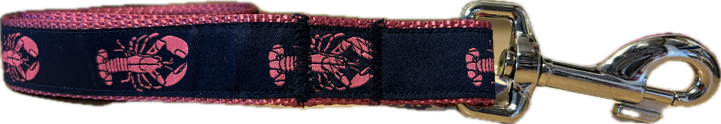 A horizontal view of a dog leash featuring a dark navy blue fabric ribbon with a repeating pink lobster pattern, stitched onto contrasting vibrant pink nylon webbing and attached to a silver metal swivel snap hook.