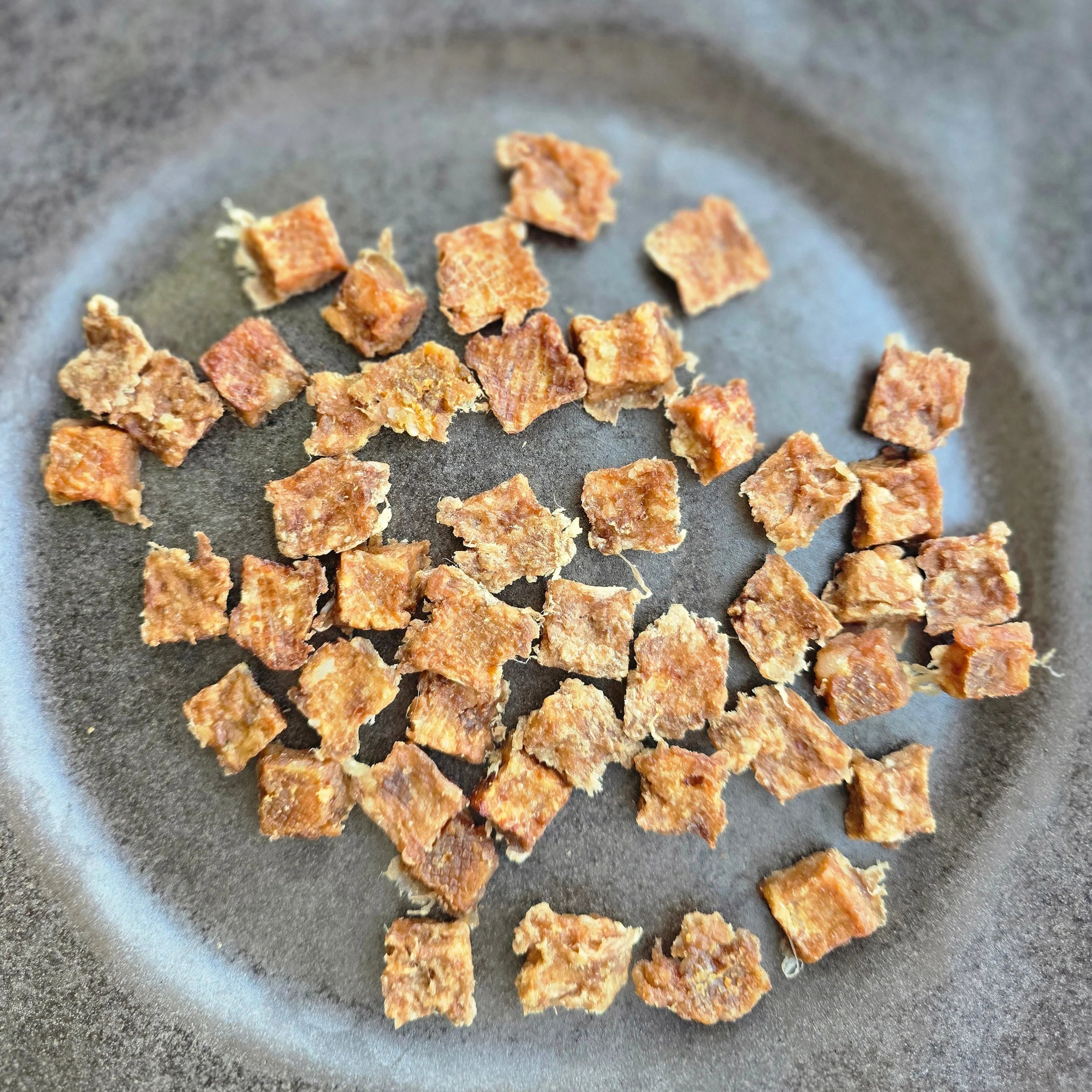 Close up of dehydrated rabbit treats for dogs on a grey plate.
