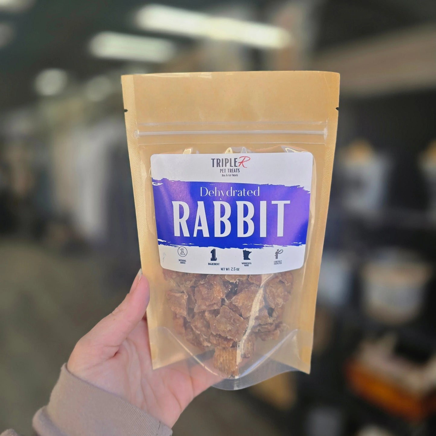 Hand holding a package of dehydrated rabbit dog treats with a blurred background